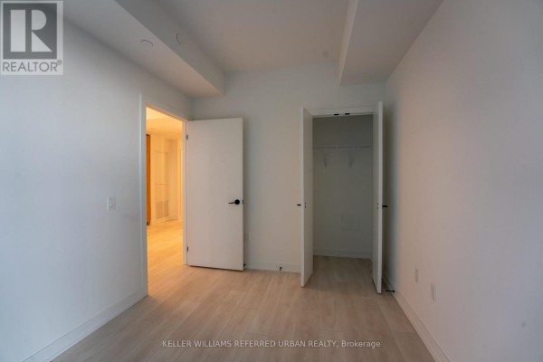 Bedroom with light wood floors, white walls, open closet, and doors to hallway and another room. - N1301 - 117 Broadway Avenue N, Toronto