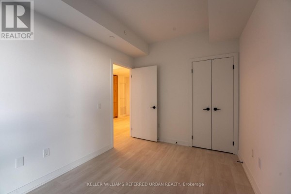 View of a bedroom with light wood floors, white walls, and two doors, one opening to a hallway. - N1301 - 117 Broadway Avenue N, Toronto