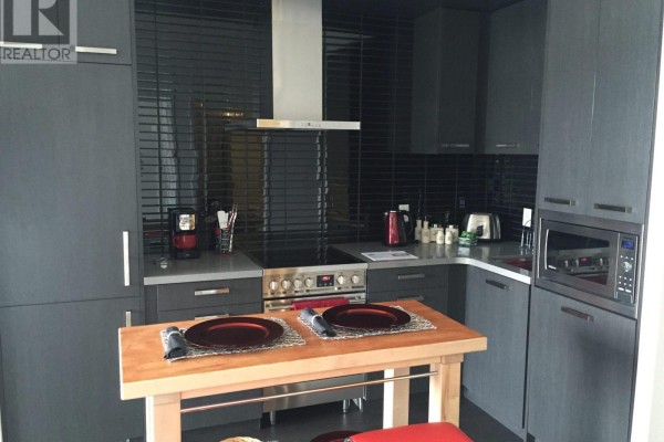 Kitchen island with two place settings and view of grey cabinets and appliances. - N222 - 120 Bayview Avenue, Toronto