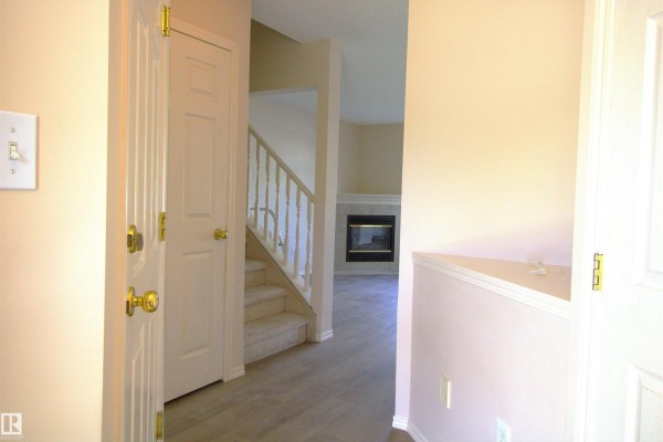 Interior hallway view with beige walls, wood-look flooring, and staircase leading upstairs. - #26 13403 Cumberland Rd Nw, Edmonton