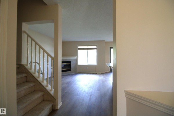 View from hallway into living room with fireplace, large window, and staircase on the left. - #26 13403 Cumberland Rd Nw, Edmonton