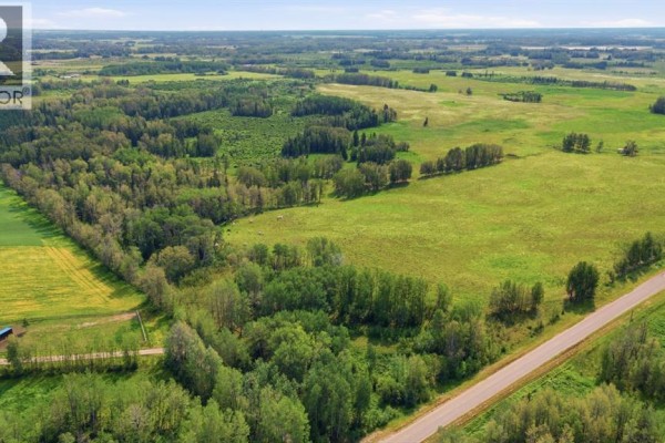 Aerial view of a paved road running through a landscape of green fields and dense trees. - On Range Road 45, Rural Clearwater County