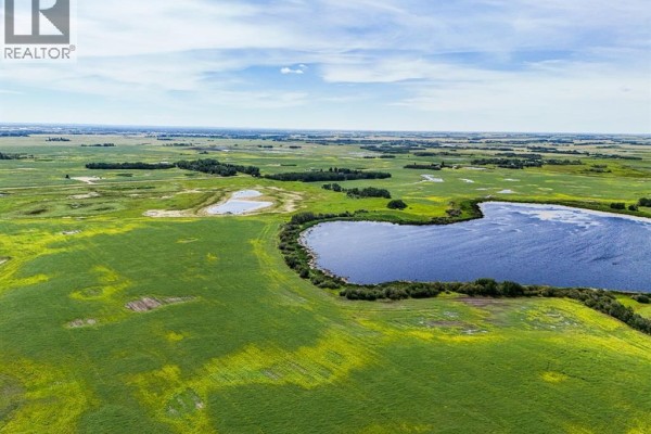 Expansive aerial view of green farmland dotted with bodies of water under a partly cloudy sky. - On Township Road 474, Rural Camrose County
