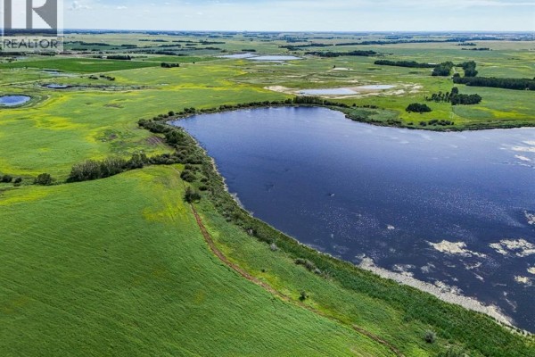 Aerial view showcasing a large, dark blue pond bordering a green field and distant agricultural land. - On Township Road 474, Rural Camrose County
