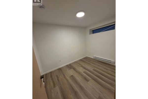 Bedroom with light wood flooring, white walls, a small window, and a white baseboard heater. - One Bedroom Basement-xx W 63 Avenue, Vancouver