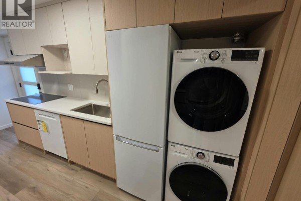 Stacked white LG washer and dryer next to a white refrigerator in the kitchenette area. - One Bedroom Basement-xx W 63 Avenue, Vancouver