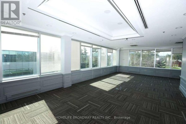 Empty office space with large windows offering a view of trees and surrounding buildings. - Opt A - 2365 Matheson Boulevard E, Mississauga