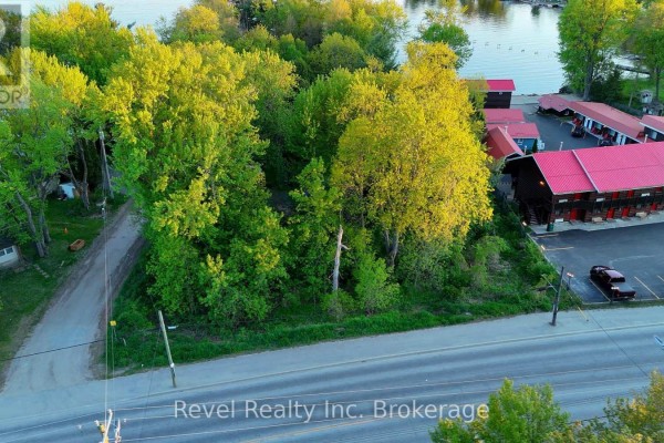 Overhead drone view of a wooded vacant lot next to a motel with red roofs and waterfront access. - Part Lot 99 Lakeshore Drive, North Bay