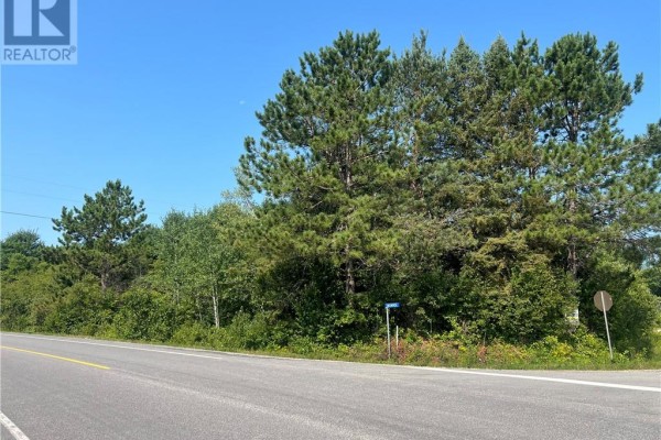 View of a wooded corner property with signs on Munro Road under a blue sky. - Pcl 24715, 25177, 15935 Munro Road, West Nipissing