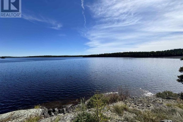 Expansive view of a wide, dark blue lake bordered by a dense forest under a partly cloudy sky. - Pcl 8 Sec Dog Lk, District Of Algoma