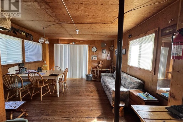 Interior view of a small cottage with wood-paneled walls, a sofa, dining table, and sliding glass doors. - Pcl 8 Sec Dog Lk, District Of Algoma