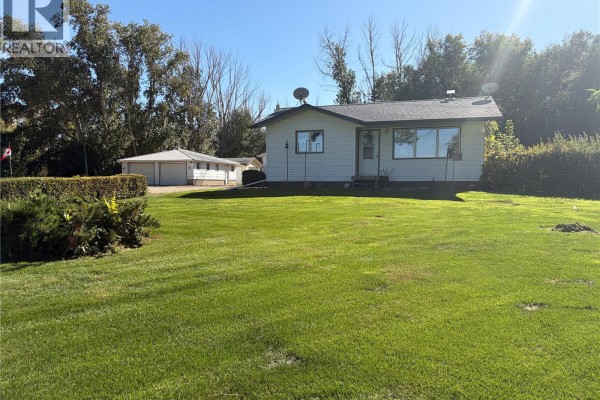 Side view of a white bungalow with a large green lawn in the foreground and a detached garage on the left. - Peterson Acreage, Big Quill Rm No  308