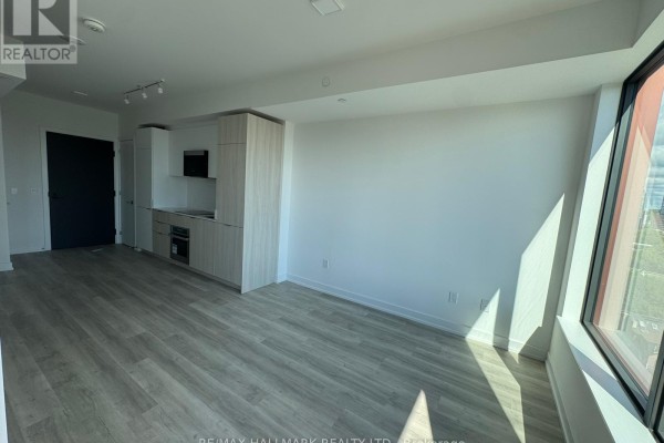 View of an empty apartment living area with a kitchen, modern cabinets, and floor-to-ceiling window. - Ph04 - 28 Eastern Avenue, Toronto