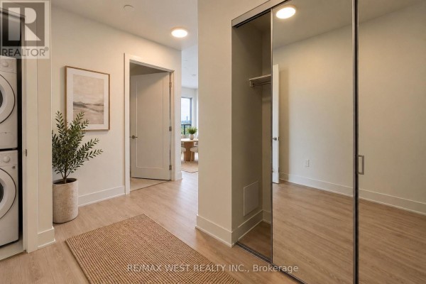 Apartment hallway with a stacked washer-dryer unit, light wood floors, and mirrored closet doors. - Ph04 - 858 Dupont Street, Toronto