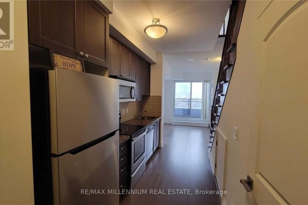 Interior view of a narrow kitchen with dark wood cabinets, stainless steel appliances, and a stairway on the left. - Ph08 - 1060 Sheppard Avenue, Toronto