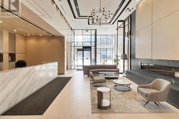 Apartment building lobby with a marble reception desk, seating area, and modern chandelier. - Ph09 - 1 Belsize Drive, Toronto