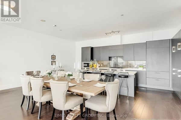 Dining area with a large wooden table and chairs, adjacent to a grey modern kitchen. - Ph1302 - 39 Queens Quay E. Street E, Toronto