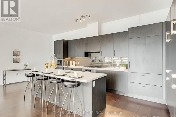 Modern kitchen island with a sink and bar stools, facing grey cabinetry and backsplash. - Ph1302 - 39 Queens Quay E. Street E, Toronto