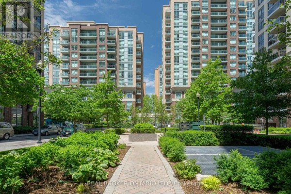 Pathway through a manicured garden area with lush green plants and trees. - Ph2 - 3 Michael Power Place, Toronto
