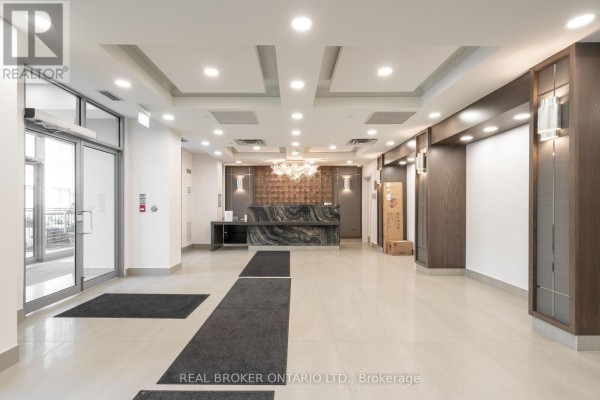 Spacious apartment building lobby with a marble reception desk and modern lighting. - Ph2 - 3 Michael Power Place, Toronto