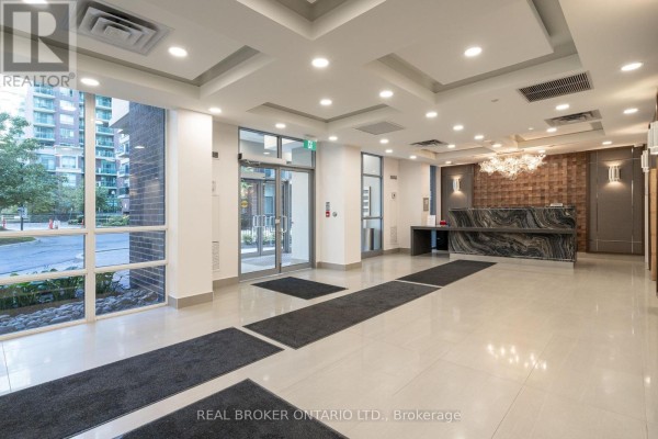 Bright apartment lobby with large windows overlooking the exterior, a reception desk, and seating area. - Ph2 - 3 Michael Power Place, Toronto