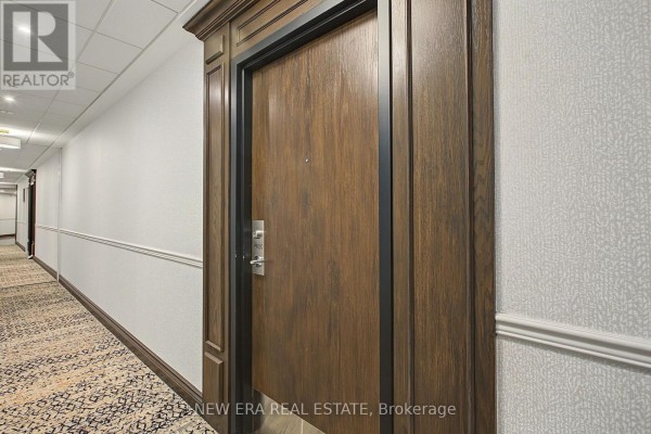 Hallway with carpeted floor, white paneled walls, and a close-up of a wood apartment door. - Ph20 - 8201 Islington Avenue, Vaughan