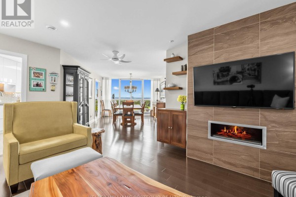 Living and dining area with dark hardwood floors, fireplace, TV, and large windows with view. - Ph208 - 2 Westney Road N, Ajax