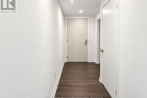 Hallway with white walls, dark wood floor, and a light wood door. - Ph2408 - 30 Samuel Wood Way, Toronto