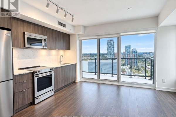 Kitchenette with dark wood cabinets, stainless steel appliances, and city view. - Ph2408 - 30 Samuel Wood Way, Toronto