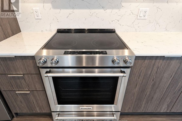 Close-up of a stainless steel electric stove with a dark wood cabinet. - Ph2408 - 30 Samuel Wood Way, Toronto