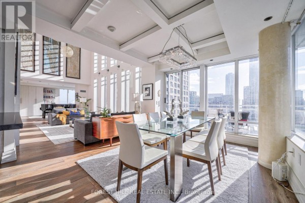 Dining room with a glass table, eight white chairs, and a crystal chandelier, overlooking the city. - Ph2701 - 8 Colborne Street, Toronto