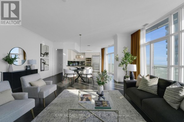 Open-concept layout featuring a dark sofa, light rug, and dining area with city views. - Ph3 - 50 Absolute Avenue, Mississauga