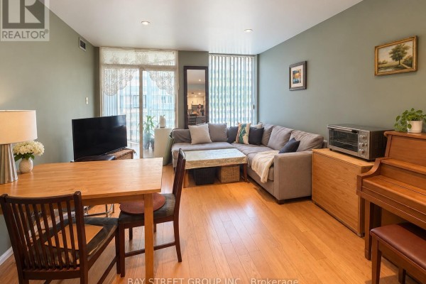 Living and dining area with sectional sofa, wooden dining table, piano, and hardwood floors. - Ph7 - 701 King Street W, Toronto