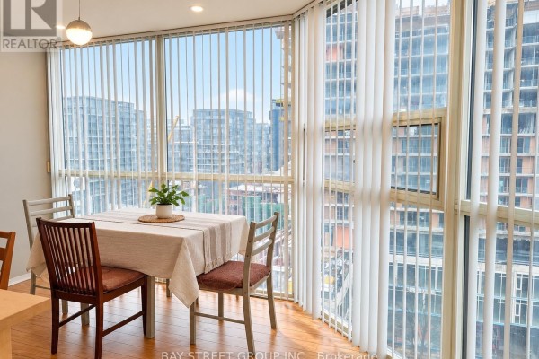 Dining area with table and chairs beside large floor-to-ceiling windows overlooking city buildings. - Ph7 - 701 King Street W, Toronto