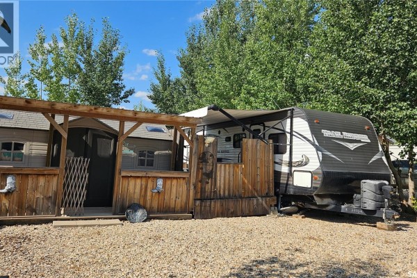 Outdoor seating area with wooden structures next to a travel trailer in a treed setting. - Prairie Sky Drive, Lucien Lake
