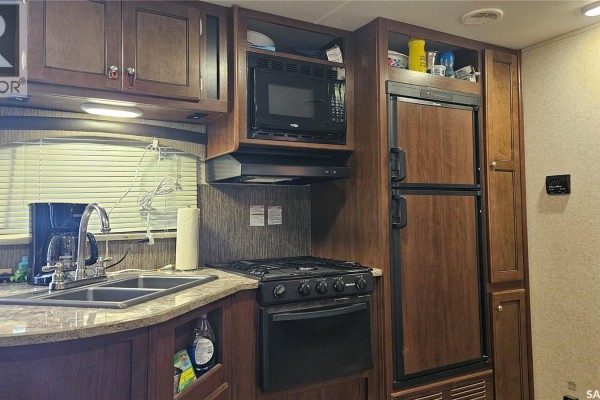 RV kitchen with wooden cabinets, granite counters, double sink, stove, microwave, and refrigerator. - Prairie Sky Drive, Lucien Lake