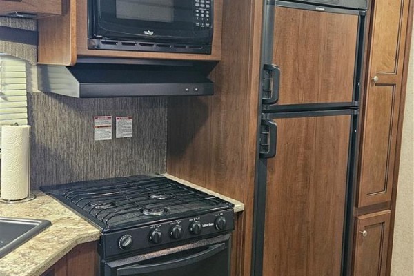 Close-up of an RV propane stove and oven below a microwave and above dark wood cabinets. - Prairie Sky Drive, Lucien Lake