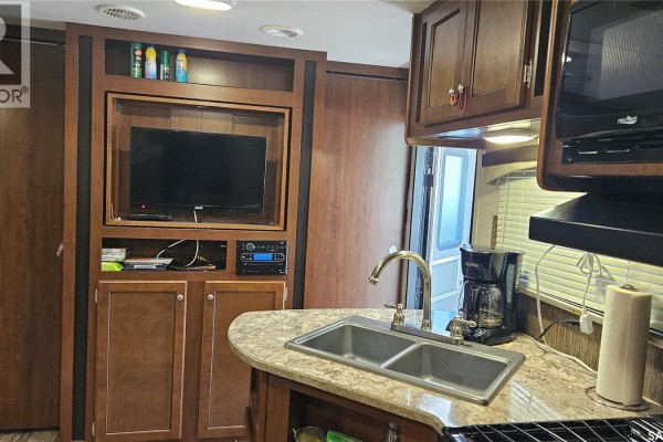 Interior RV living space with wood cabinets, television, entertainment center, sink, and counter. - Prairie Sky Drive, Lucien Lake