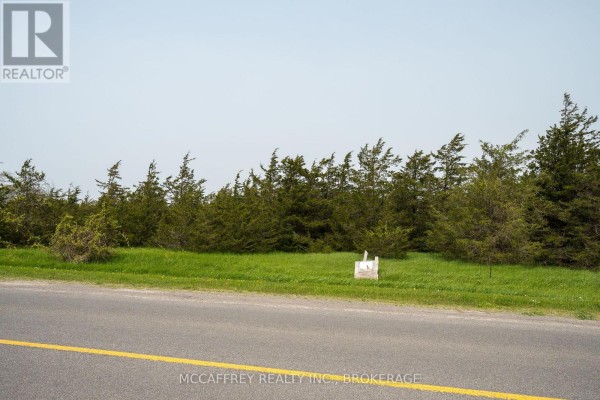 View of a treeline with grass and a white signpost along a paved road. - Pt Lt63 County Rd 7, Prince Edward County