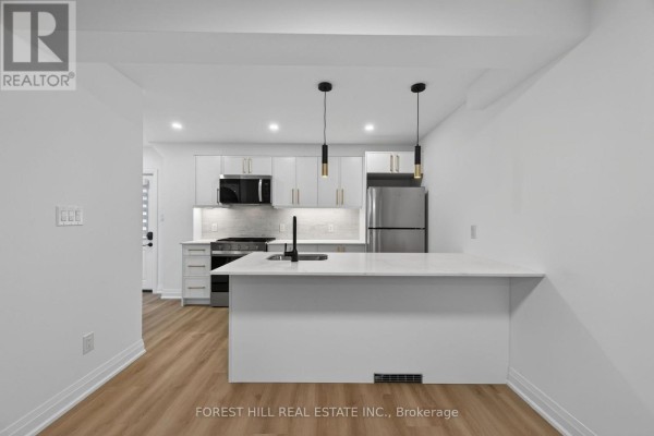 Kitchen with white island, light grey cabinets, and stainless steel appliances. - R - Garden - 221 Churchill Avenue, Toronto