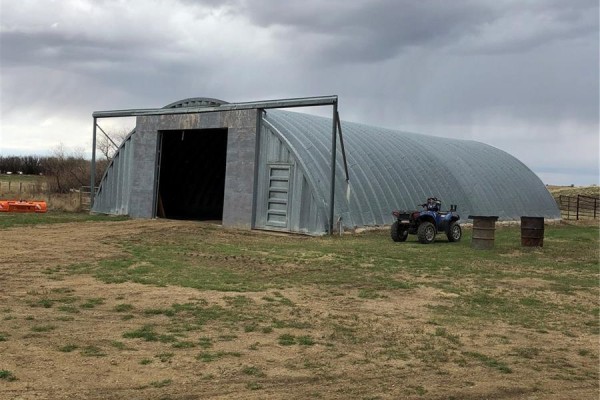 Large quonset hut with an open bay door, an ATV parked outside, and two barrels. - Rapley Arena Quarter, Val Marie Rm No  17