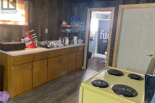 Kitchen area with light wood cabinets, a double sink, a yellow stove, and an open doorway to a bathroom. - Rapley Arena Quarter, Val Marie Rm No  17