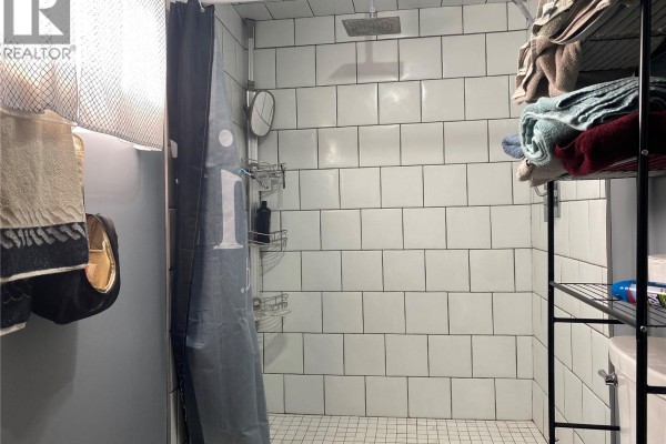 Shower stall with white subway tiles, a grey shower curtain, and stacked towels on a shelf. - Rapley Arena Quarter, Val Marie Rm No  17