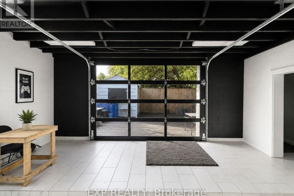 Interior space with white tiled floor, black walls, and a large glass overhead door opening to a backyard. - Rear - 313 Horton Street, London East