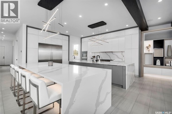 Wide view of a modern white and grey kitchen with a large quartz island, seating, and built-in shelving. - Regina View Acreage, Sherwood Rm No  159