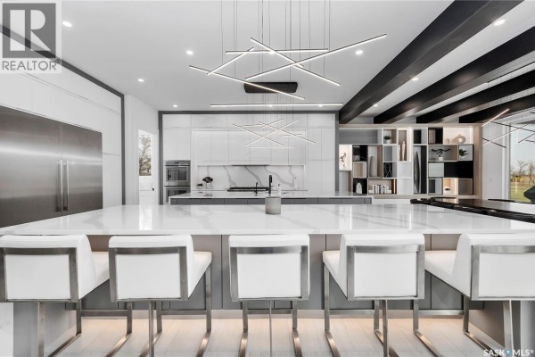 Close-up of a modern white and grey kitchen island with white stools and a view of open shelving. - Regina View Acreage, Sherwood Rm No  159