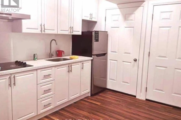 A small kitchen with white cabinets, stainless steel refrigerator, and dark wood flooring. - Renovated Bedroom Bsmt - 16 Ross St Street, Toronto
