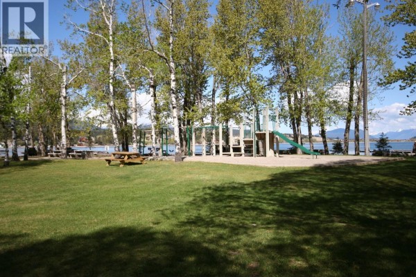 Grassy park area with picnic tables, trees, and a playground, with water in the distance. - Ridge Way Lot# 114, Windermere