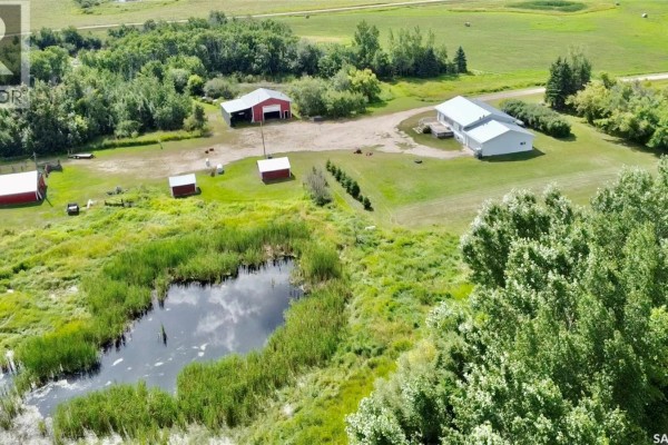 Aerial view of farm buildings including a white house, red barn, and smaller sheds, adjacent to a pond and trees. - Rm Of Kellross Farm, Kellross Rm No  247