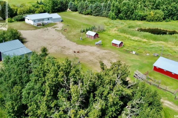 Aerial view of farm property with multiple outbuildings, a fenced area, trees, and a pond reflecting the sky. - Rm Of Kellross Farm, Kellross Rm No  247